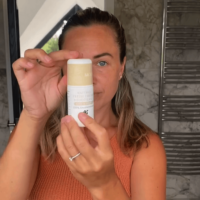 Woman applying MooGoo Fresh Cream Deodorant Oats and Honey, MooGoo Fresh Cream Deodorant Lemon Myrtle displayed on clean white backdrop, natural roll-on with light citrus fragrance and alkaline formula, natural roll-on formula to control odour without irritation.