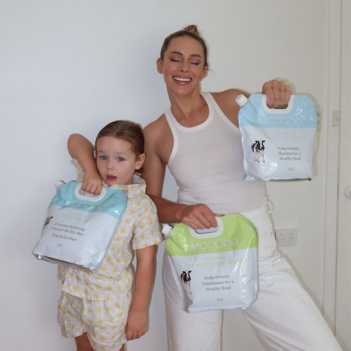 MooGoo Shampoo and Conditioner refill packs held up by woman and child, natural silicone free bulk haircare for healthy scalp and family use