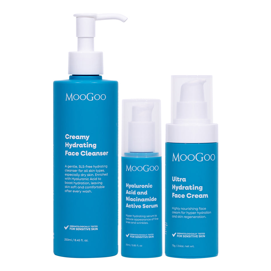 Three blue MooGoo skincare bottles on a white background: a large face cleanser pump bottle, a smaller serum bottle, and a hydrating face cream pump bottle.